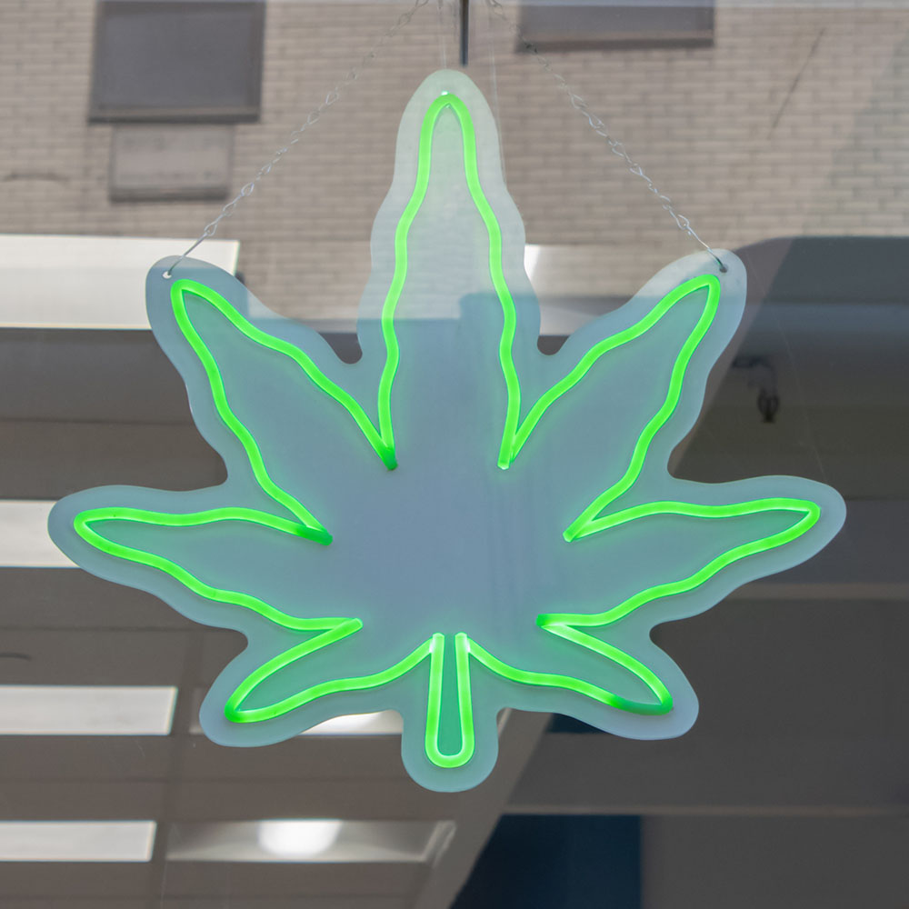 Neon sign of the outline of a cannabis leaf in a store window
