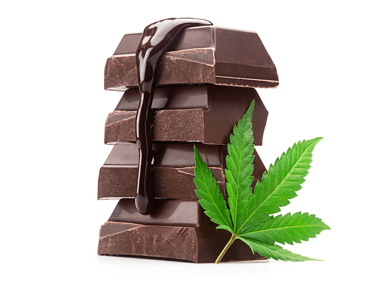 Stack of chocolate bar squares with chocolate sauce dripping down, sitting on top of a cannabis leaf