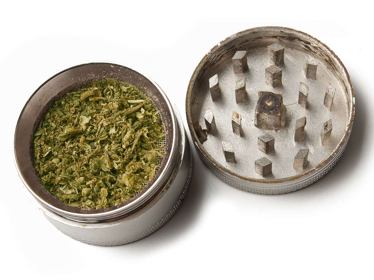 Two-piece grinder laying open with ground cannabis on one side