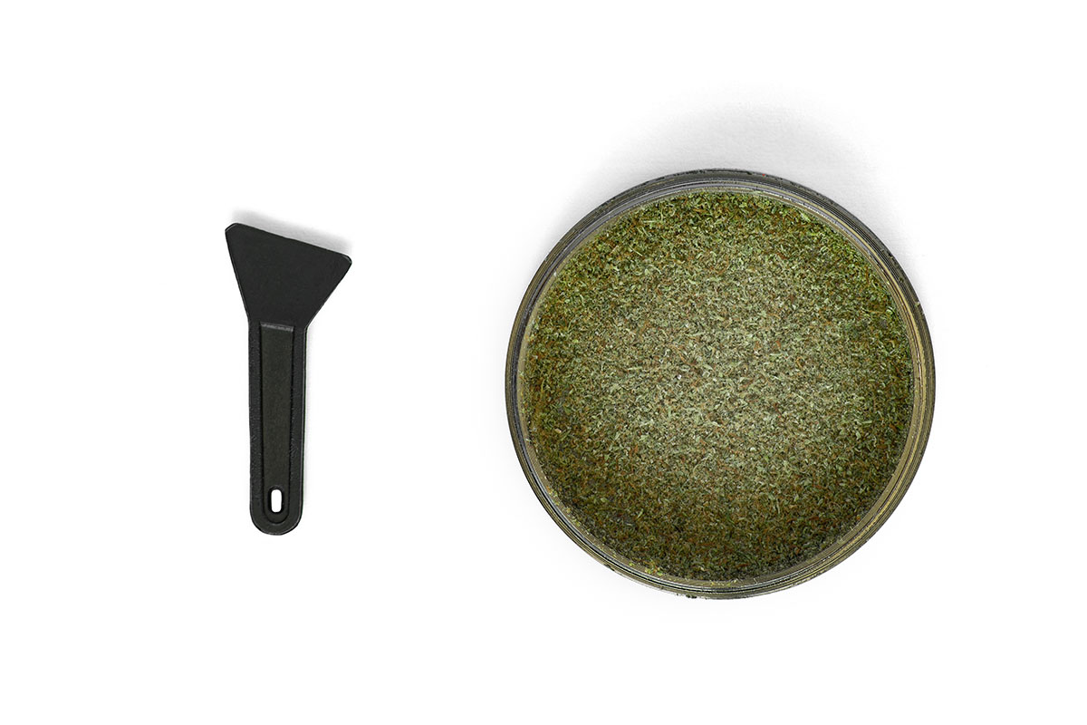 Bottom of a grinder filled with kief next to a kief spatula