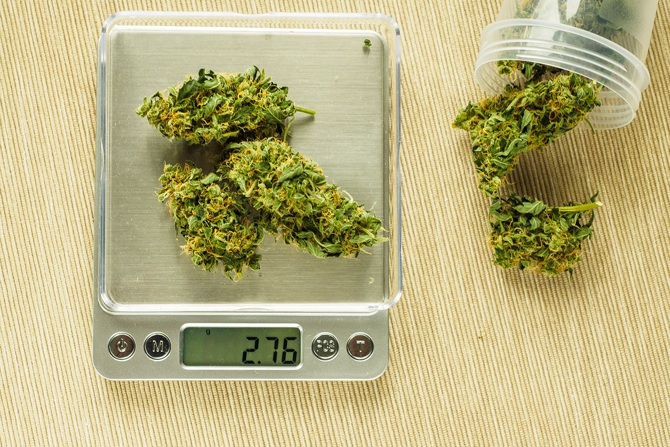 cannabis flower on a metal scale next to a plastic jar of cannabis flower