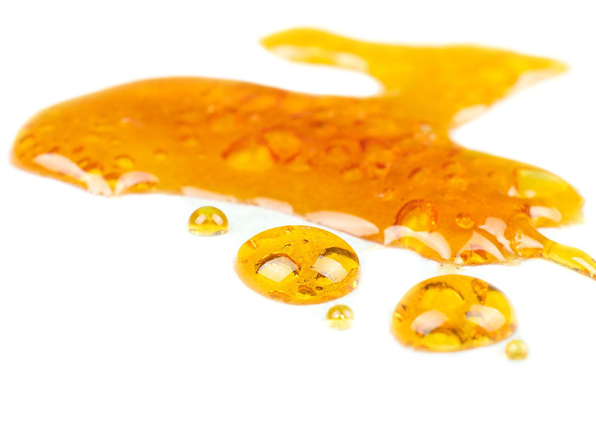 Golden liquid cannabis concentrate spread on a white background