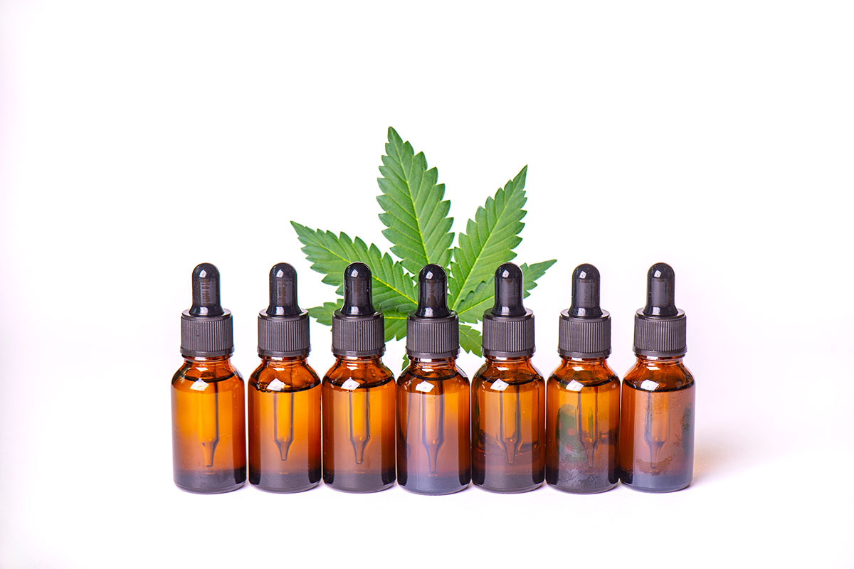 Seven opaque tincture bottles lined up in front of a cannabis leaf